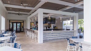 A covered outdoor dining area with multiple tables and chairs, a central bar area with a counter, and a ceiling with recessed lighting and fans.
