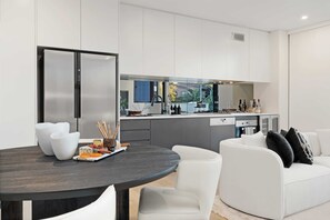 A modern kitchen with a dining area, white furniture, and a view of the outdoors. - The Loft by Coast Hosting (Terrigal)