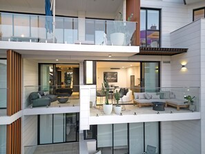 A modern multi-level apartment with glass railings, a dining area, and a living room with sofas and potted plants. - Art-Filled Loft: 50m Beach, King, Parking (Terrigal)
