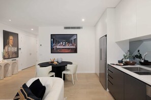 A modern kitchen with a dining area, white cabinetry, and a large framed artwork above the dining table. - The Loft by Coast Hosting (Terrigal)