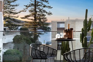 Ein Balkon mit zwei Stühlen, einem Tisch und einer Flasche, mit Blick auf ein Gewässer und Gebäude.