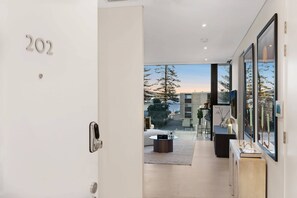 A modern interior with a door labeled '202,' a view of the outdoors, and a minimalist living area with a coffee table and a side table. - Art-Filled Loft: 50m Beach, King, Parking (Terrigal)