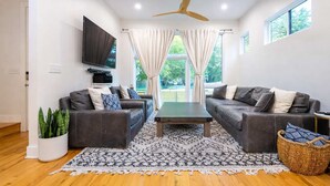 Uma sala de estar moderna com dois sofás, uma mesa de centro, uma TV e um ventilador de teto.
