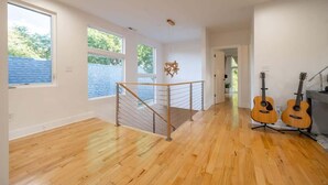 Quarto amplo com piso de madeira, janelas grandes, escada com corrimão de metal e duas guitarras encostadas na parede.