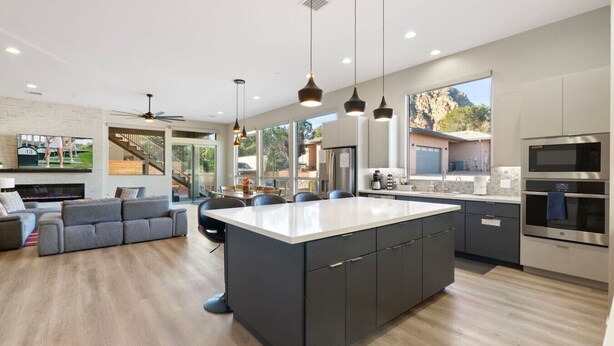 Une cuisine moderne dotée d’un grand îlot central, de meubles de couleur sombre et d’appareils électroménagers en acier inoxydable.
