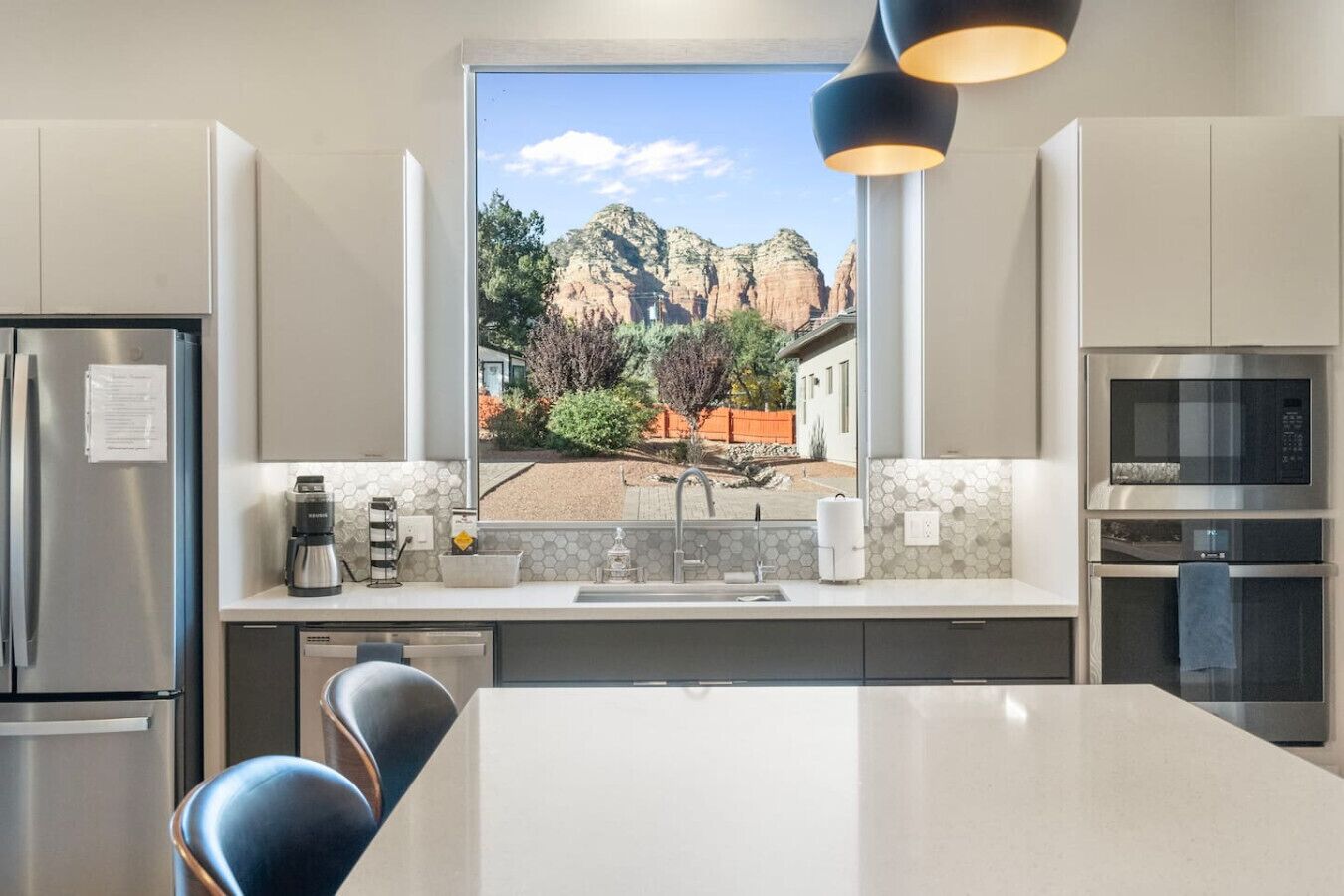 Una cucina moderna con un'isola grande, elettrodomestici in acciaio inossidabile e vista su un paesaggio montuoso attraverso una finestra.