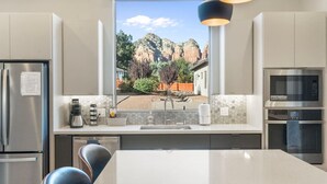 Une cuisine moderne dotée d’un grand îlot central, d’appareils électroménagers en acier inoxydable et offrant une vue sur un paysage montagneux par le biais d’une fenêtre.