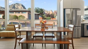 Une cuisine moderne dotée de grandes fenêtres, un coin repas avec une table et des chaises en bois, et une vue sur un paysage montagneux.