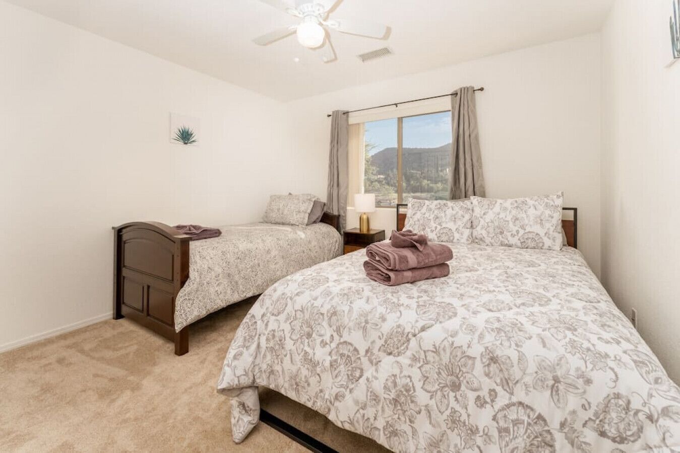 A bedroom with two single beds, a large bed, a ceiling fan, a window with curtains, and a small plant on the wall.
