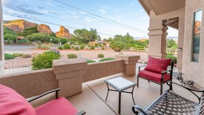 Un balcon offrant une vue sur les formations rocheuses rouges, une terrasse avec une table et des chaises, et un petit jardin.
