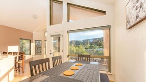 Un espace repas comprenant une longue table, des chaises et de grandes fenêtres donnant sur l’extérieur.