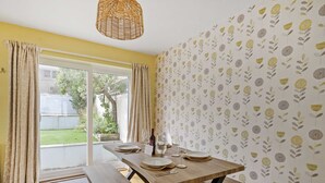 Un comedor con una mesa de madera dispuesta para dos personas, una banca y una lámpara colgante de mimbre.