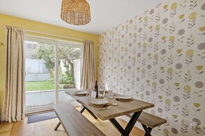 A dining area with a wooden table set for four, a wicker light fixture, and a view of a garden through a sliding door.