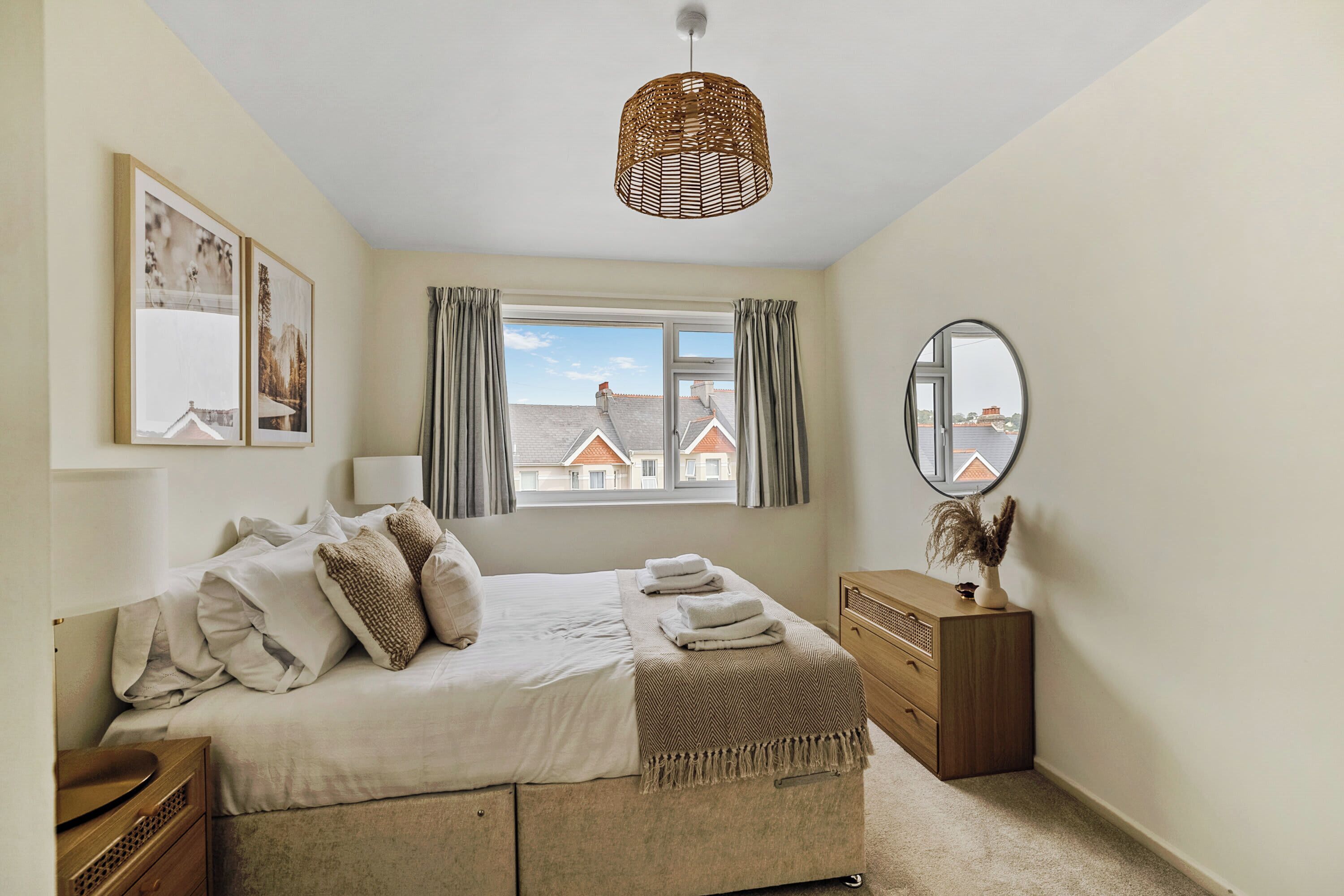 A bedroom with a bed, a dresser, a mirror, and a window with curtains.