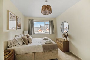 A bedroom with a bed, a dresser, a mirror, and a window with curtains.