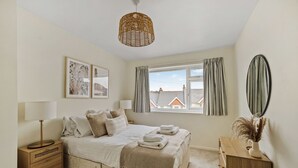 Un dormitorio con cama, mesitas de noche, lámpara, ventana con cortinas y vistas a edificios.
