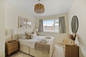 A bedroom with a bed, bedside tables, a dresser, a window with curtains, and a hanging light fixture.