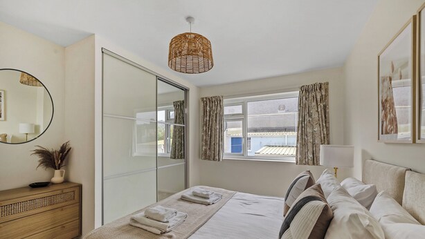 Un dormitorio con cama, mesita de noche, lámpara, espejo, ventana con cortinas y vistas al exterior.