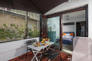 A balcony with a table set for breakfast, a bed with orange pillows, and a view of the city. - Seafront Adriatic Pearl Suite (Kraljevica)
