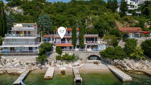 Un hotel costero con varios balcones, un puente de piedra y aguas cristalinas.