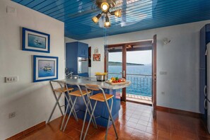 A kitchen with a central island, a dining area with bar stools, a ceiling fan, and a view of the sea through a glass door. - Adriatic Pearl Suite (Kraljevica)