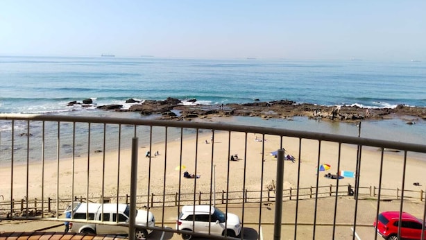 A beach view from a balcony with a railing, rocky shoreline, and several parked cars. - 316 Cozumel (eMdloti)