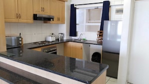 A compact kitchen with wooden cabinets, a black countertop, a stove, a sink, and a refrigerator. - 316 Cozumel (eMdloti)