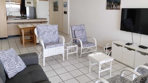 A modern living room with a sofa, two patterned armchairs, a coffee table, a TV, and a kitchen area in the background. - 316 Cozumel (eMdloti)
