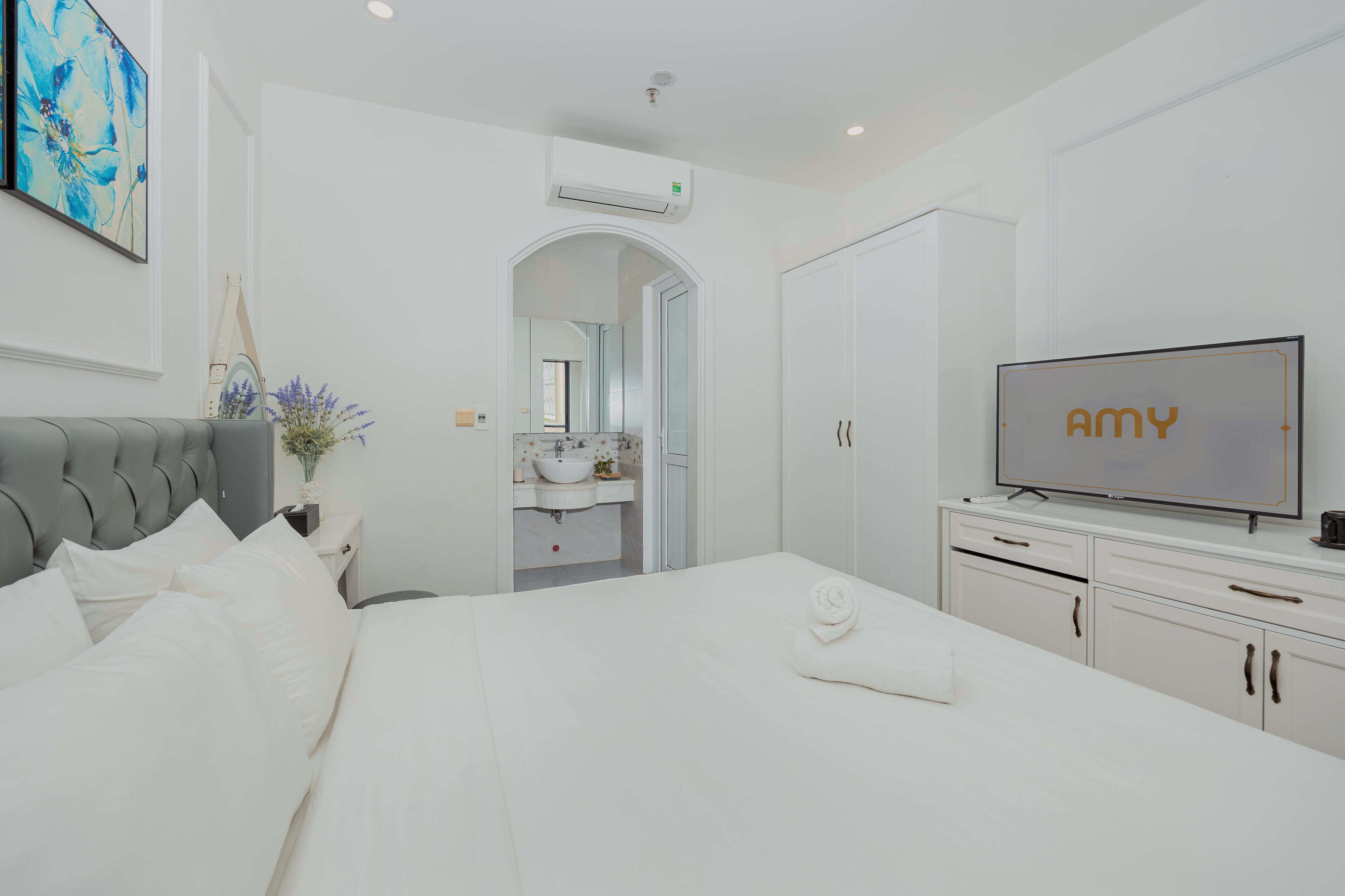 Una habitación de hotel moderna con cama, televisor, tocador con espejo y baño visible a través de un arco.
