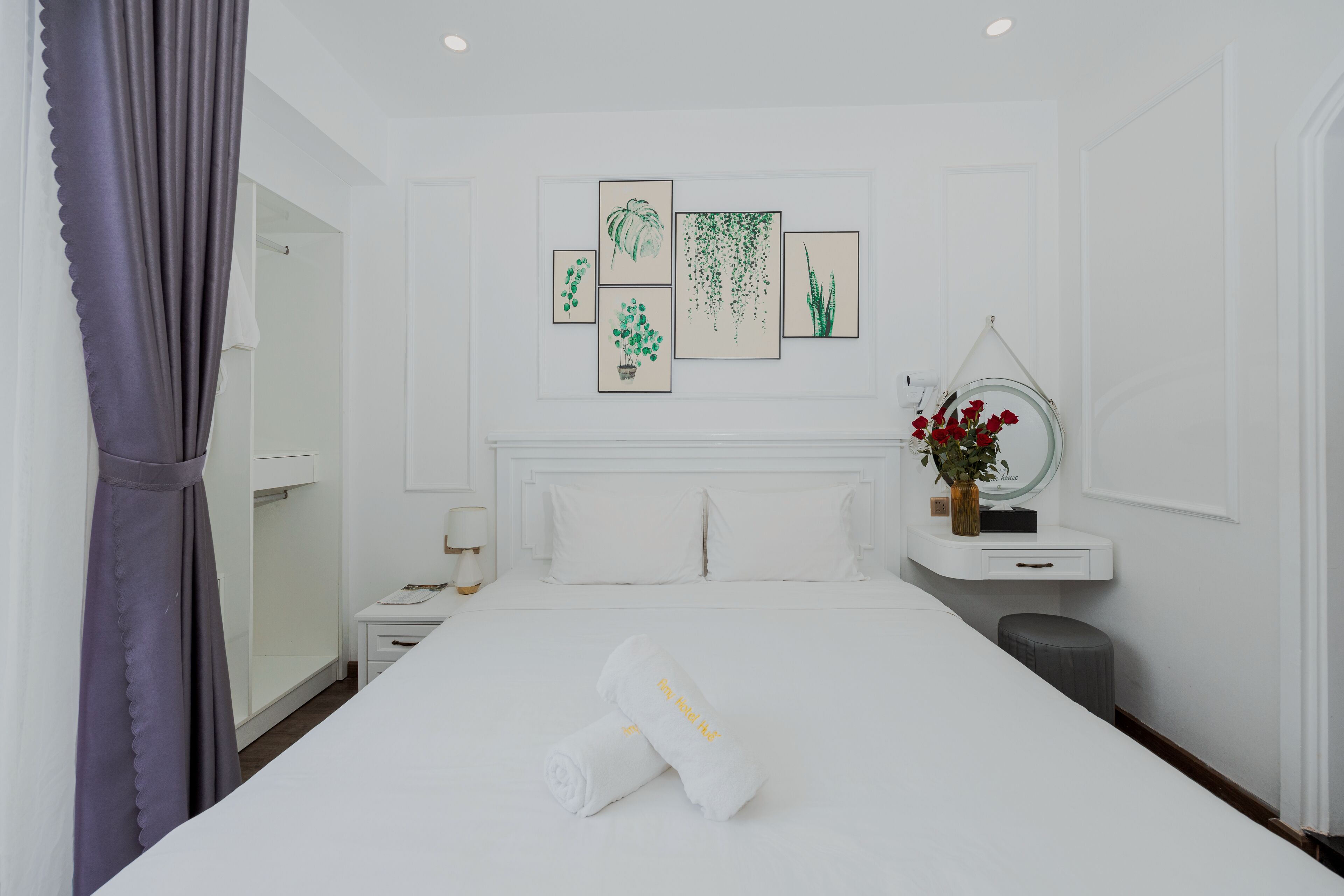 A hotel room with a bed, a nightstand, a mirror, a small table, and a window with curtains.