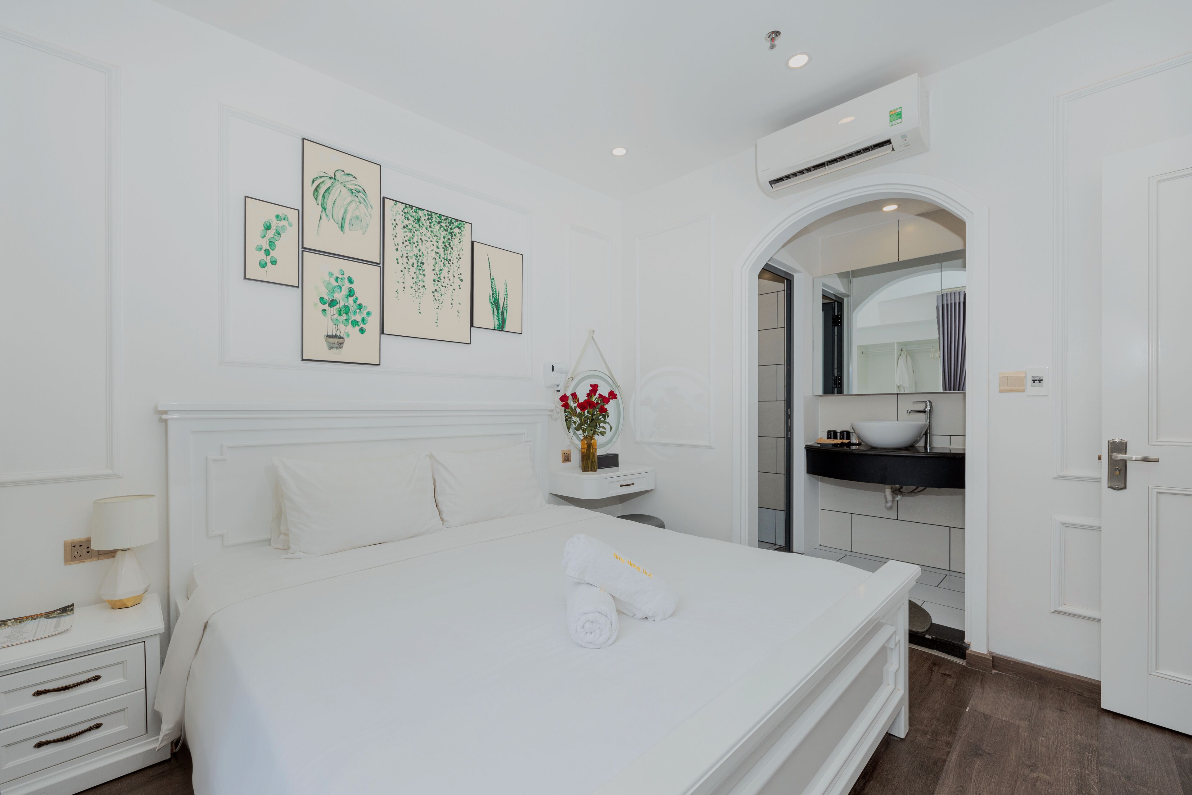 A hotel room with a bed, a bedside table, a mirror, a bathroom with a sink and mirror, and wall art.