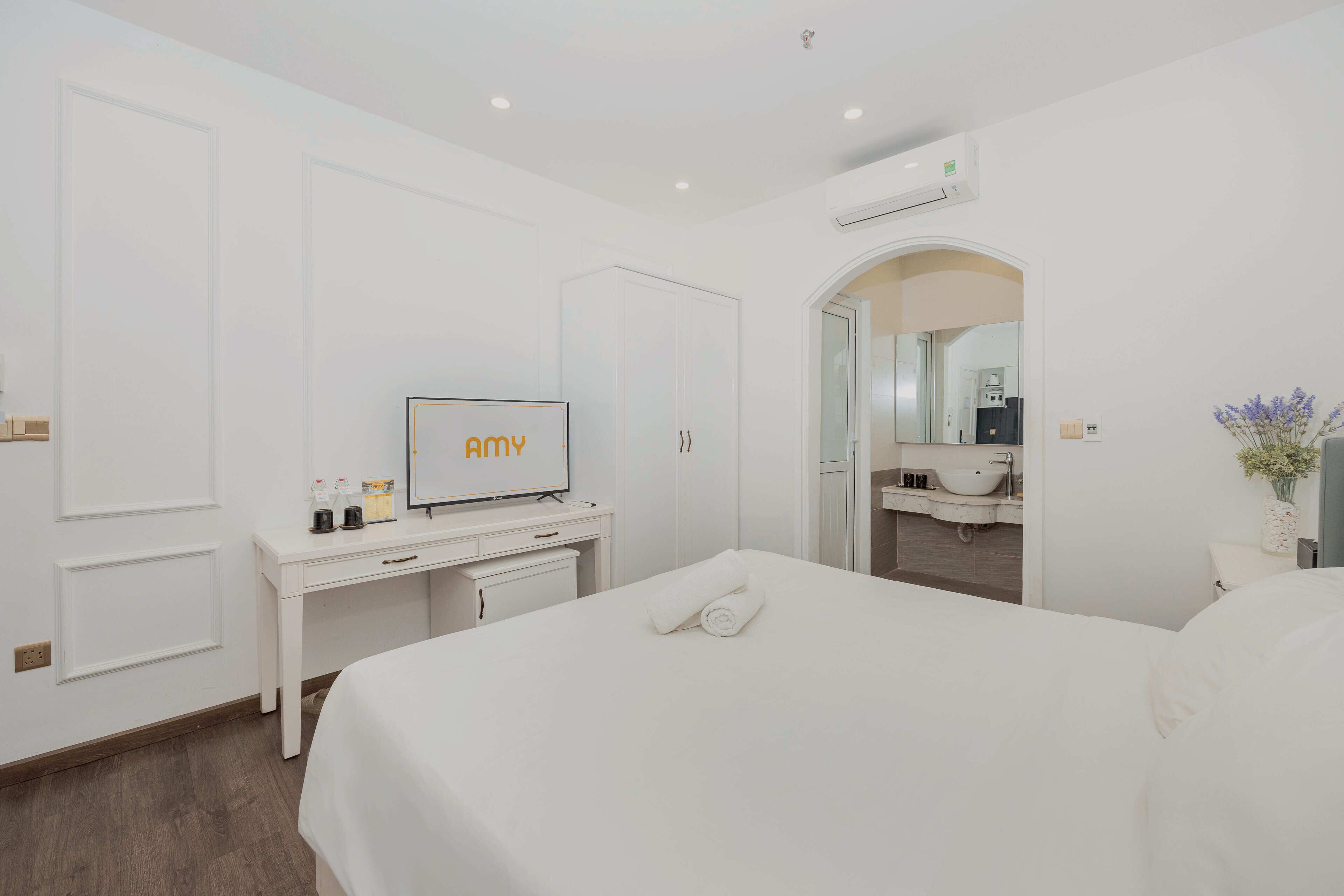 Una habitació d'hotel amb un llit, una escriptori amb televisió, un bany amb un lavabo i un mirall, i un aparell d'aire condicionat a la paret.