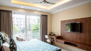 A bedroom with a bed, a desk, a TV, and a balcony with curtains. - Perch Arbor Cyber City (Gurugram)