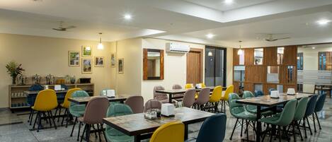 A dining area with multiple tables and chairs, an air conditioning unit, and framed pictures on the walls.