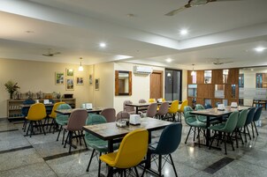 A dining area with multiple tables and chairs, an air conditioning unit, and framed pictures on the walls.