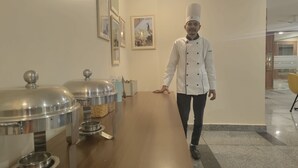 A hotel corridor with a long wooden counter, stainless steel food dispensers, and framed pictures on the wall. - Perch Arbor Cyber City (Gurugram)