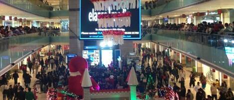 A multi-level shopping mall with a central atrium decorated with festive garlands and a large digital display.