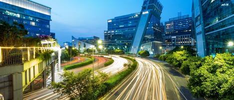 A modern urban intersection with high-rise buildings, a curved road, and light trails from moving vehicles.