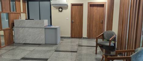 A spacious room with a marble reception desk, wooden doors, and a seating area with chairs.