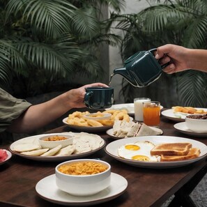 A breakfast setting with various dishes including toast, eggs, and a cup of tea being poured. - Perch Arbor Cyber City (Gurugram)