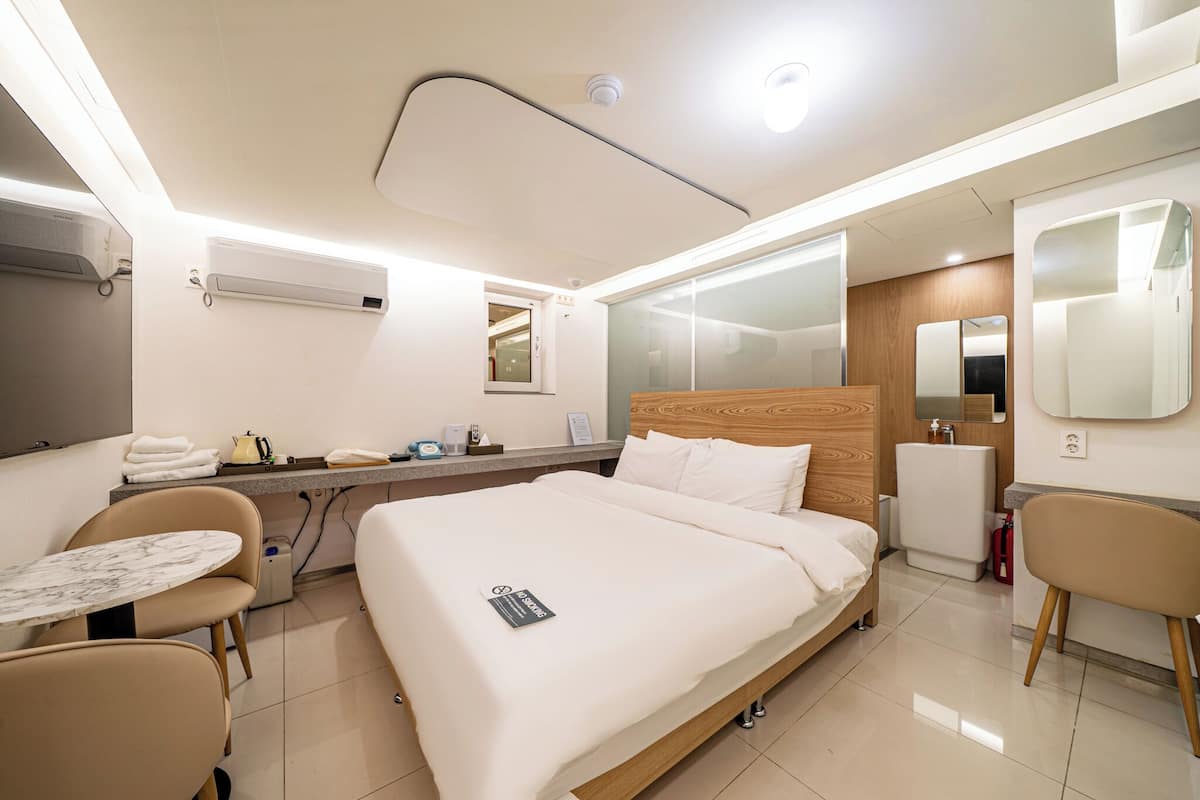 A hotel room with a bed, bedside table, chair, and a small table with a chair.
