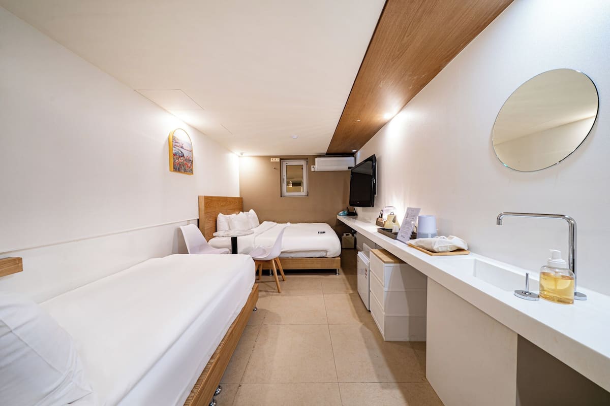 A hotel room with a single bed, a desk with a mirror, a sink, and a television.