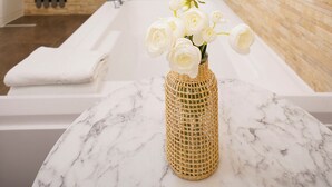 Een moderne badkamer met een marmeren wastafel, een gevlochten vaas met witte bloemen, en een stenen muur.