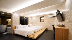 Een moderne hotelkamer met een bed, een bureau, een stoel en een aan de muur bevestigde televisie.
