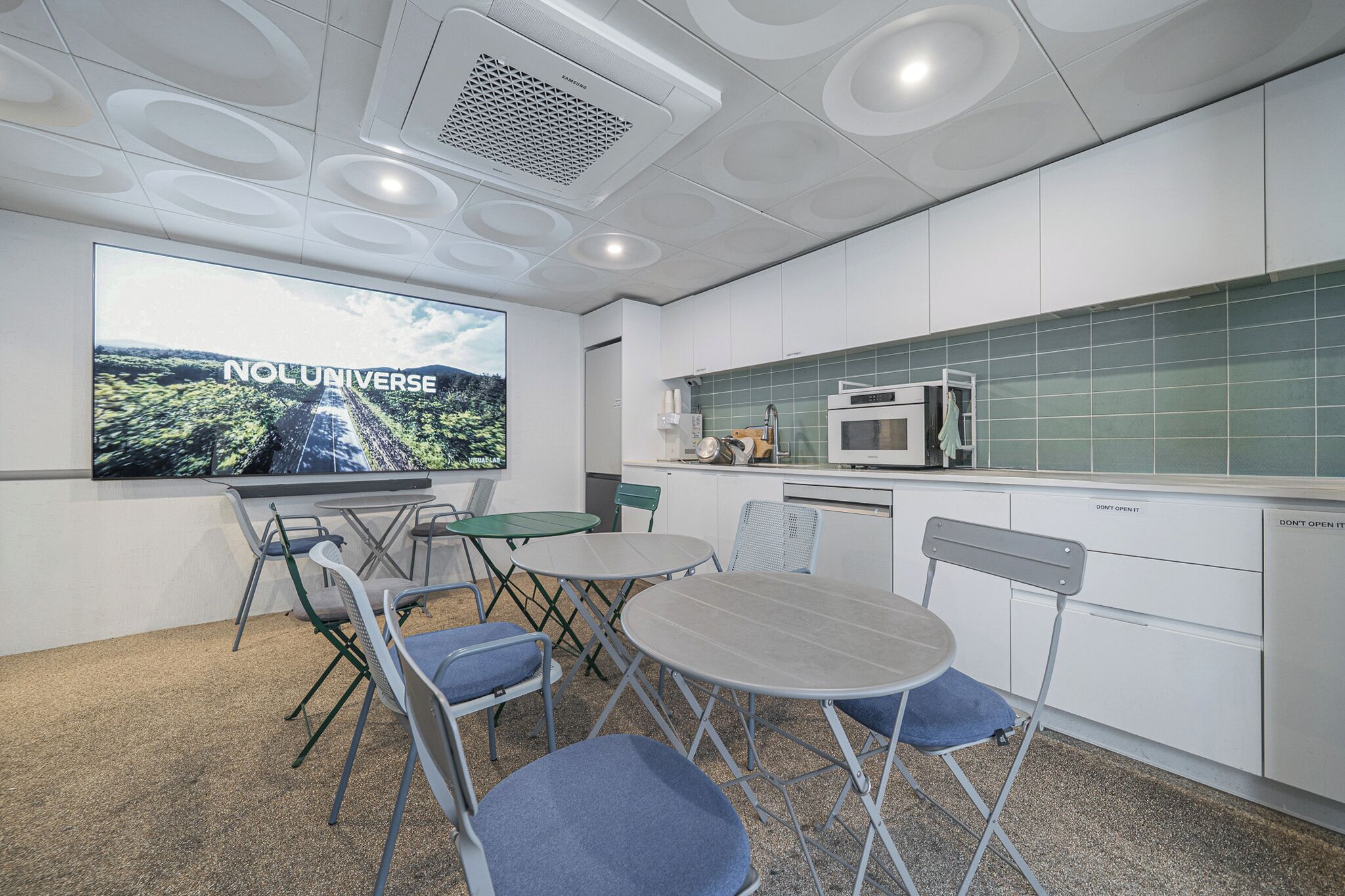 A modern kitchen with white cabinets, a microwave, and a large screen displaying "NOL UNIVERSE".