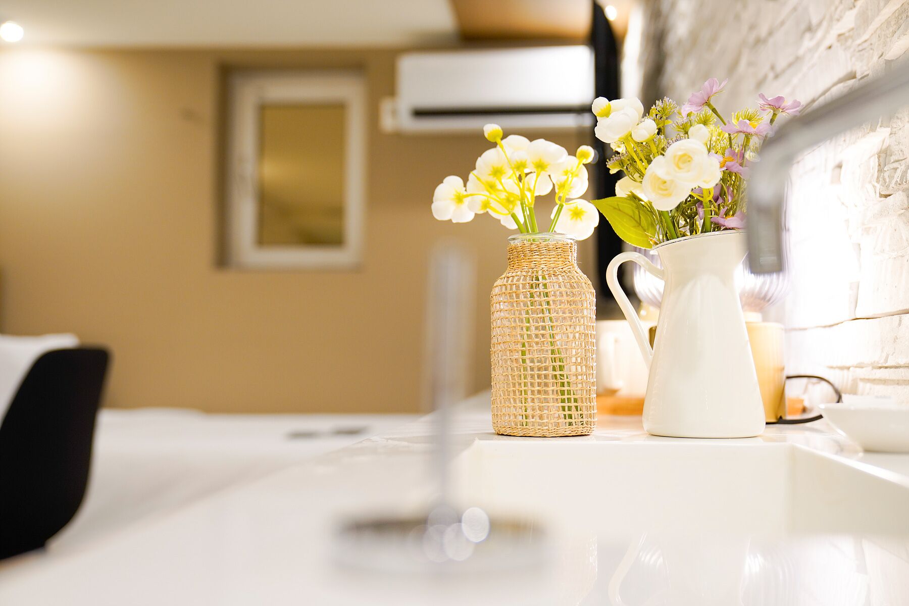 Una encimera de cocina con un florero tejido y una jarra blanca llena de flores.