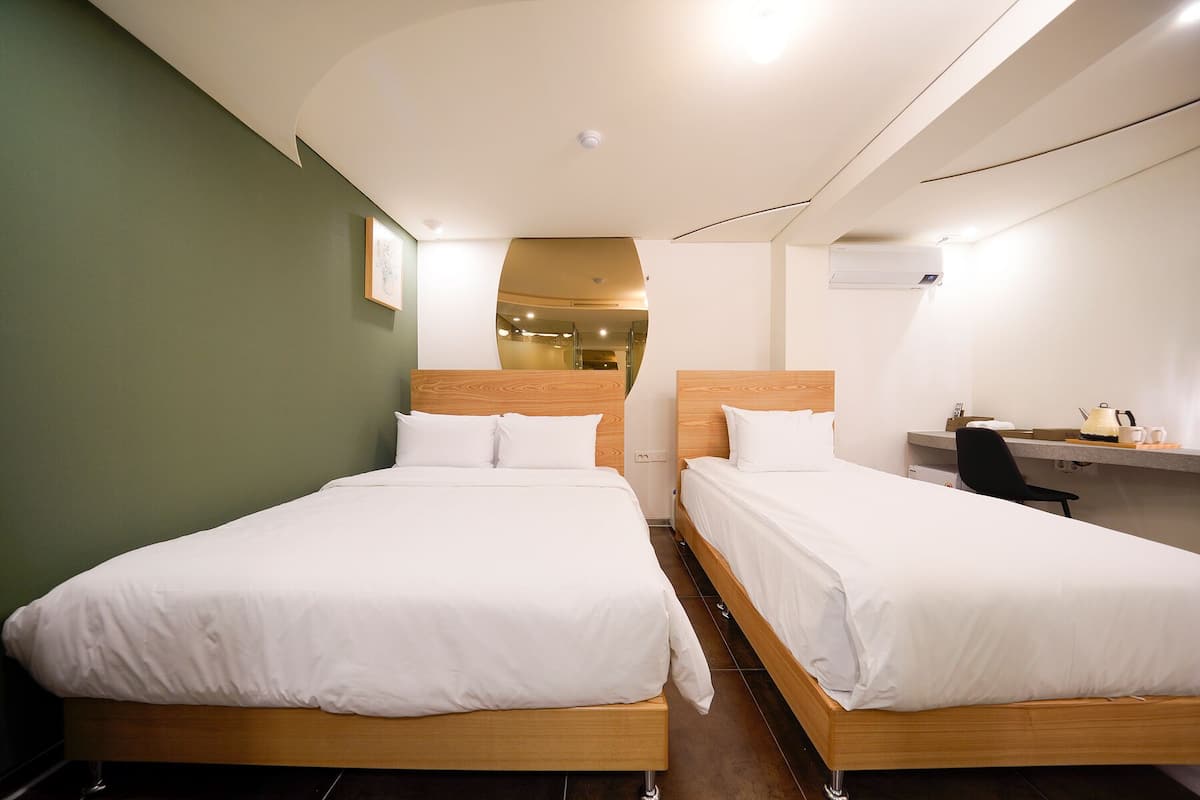 A hotel room with two wooden beds, a desk, and a chair.