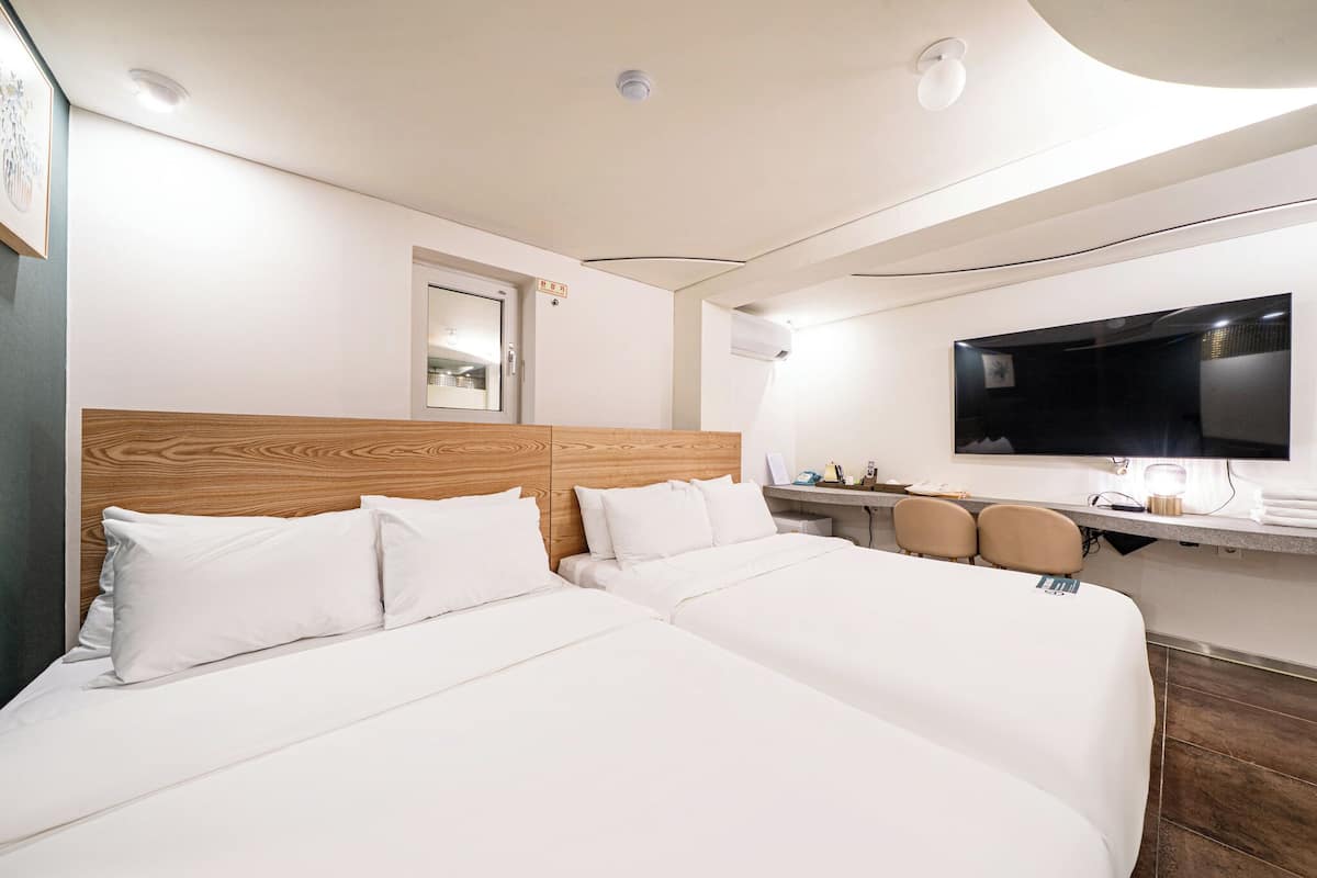 A hotel room with two beds, a wooden headboard, a flat-screen TV, a desk with chairs, and a mirror.