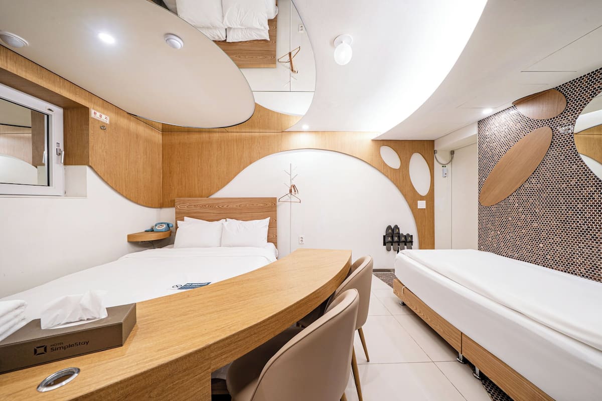A modern hotel room with a wooden desk, a bed, and a small seating area.
