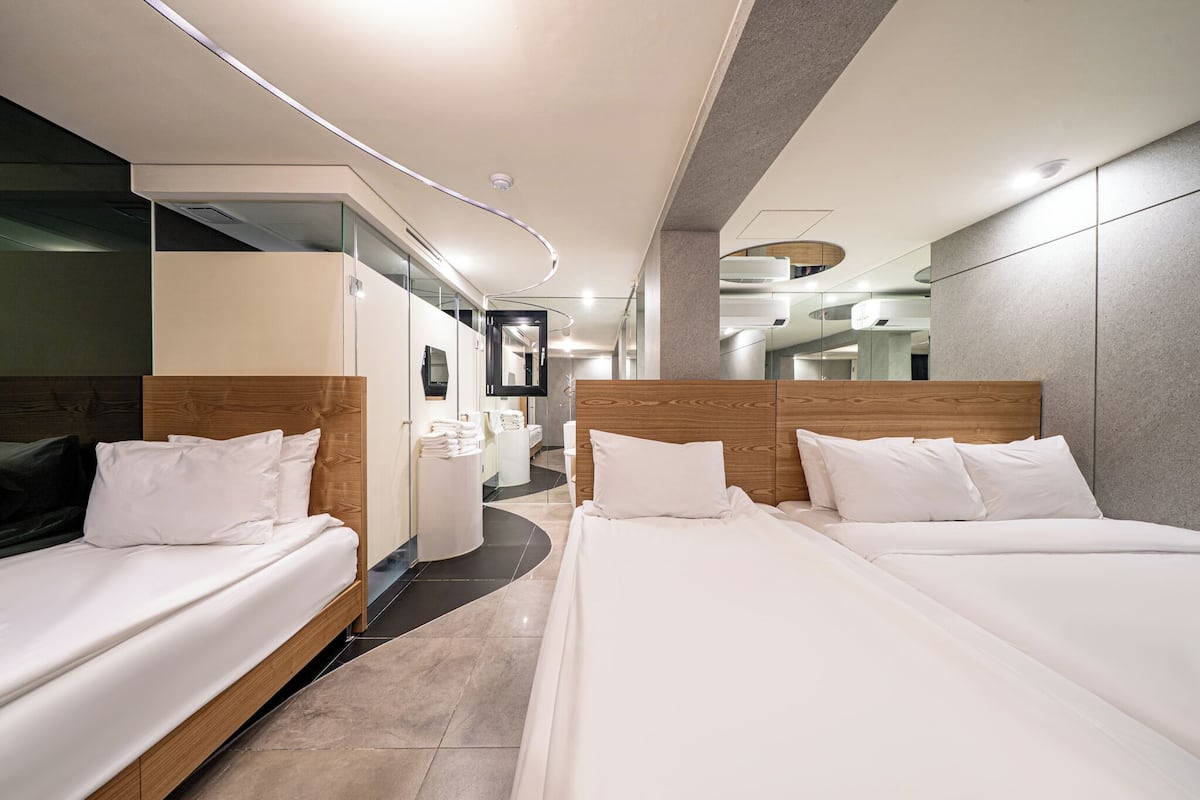A modern hotel room with two beds, a bathroom, and a mirror.